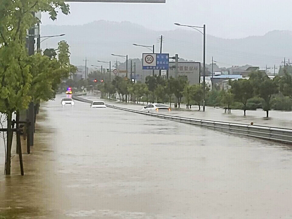▲ 폭우로 인해 양주시 만송동 도로가 깊게 침수돼 차량들이 물에 잠긴 채 멈춰 서 있다. 멀리서 경찰 차량이 경광등을 켠 채 도로를 통제하고 있다. 양쪽 도로와 가로수가 물에 잠겨 침수 피해 상황을 보여준다. /사진제공=북부소방재난본부