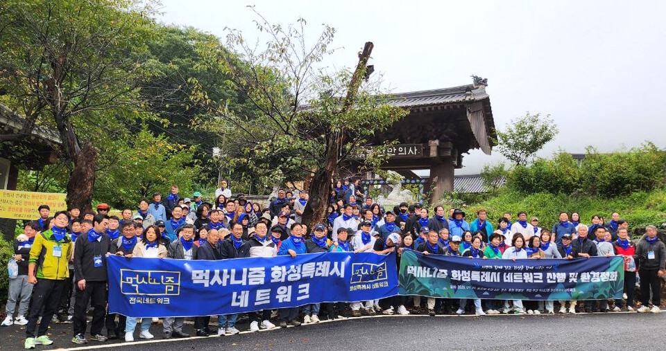 ▲ 먹사니즘 화성특례시 네트워크가 20일 화성시 동탄 무봉산 일대에서 무봉산 산행 및 플로깅 행사를 가졌다. 이날 행사에는 회원과 지역주민 등 200여명이 참여해 성황을 이뤘다. 사진은 회원들이 무봉산 만의사 입구에 집결해 단체사진을 찍고 있는 모습.