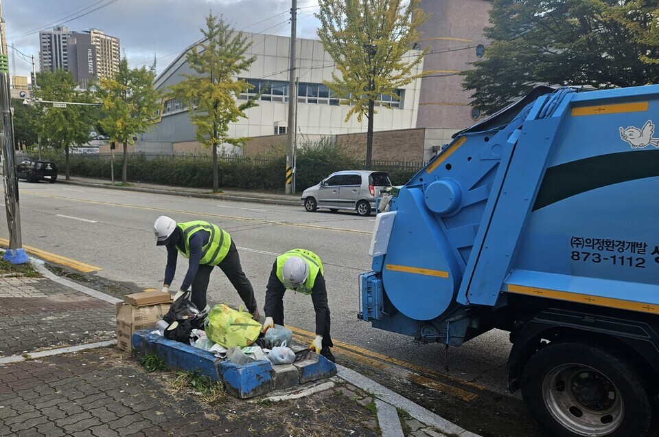▲ 지난달 23일 아침 7시경 의정부시 호원동 도로에 놓인 각종 쓰레기를 수거업체 직원들이 차량에 실어 나르고 있다.